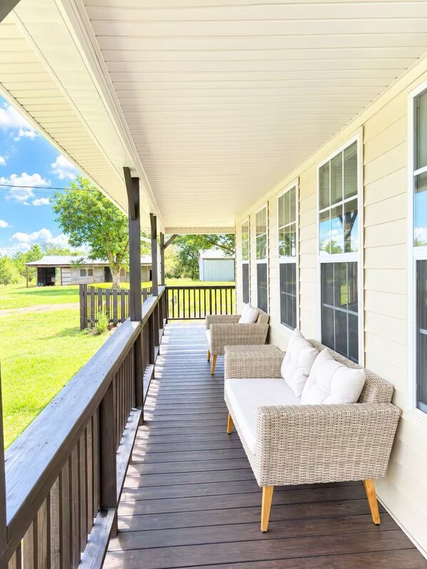 A covered porch with wicker furniture and a view of a grassy yard.