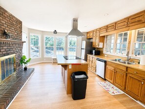 A modern kitchen with wooden cabinets, a central island, and a brick fireplace.