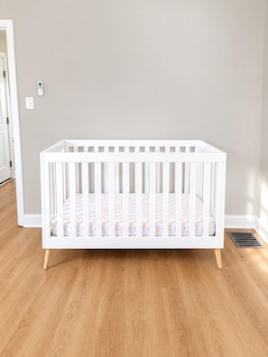 A white crib with a floral mattress in a room with light-colored walls and wooden flooring.