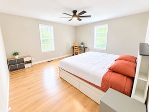 A bedroom with a bed, a desk, a chair, a ceiling fan, and two windows.