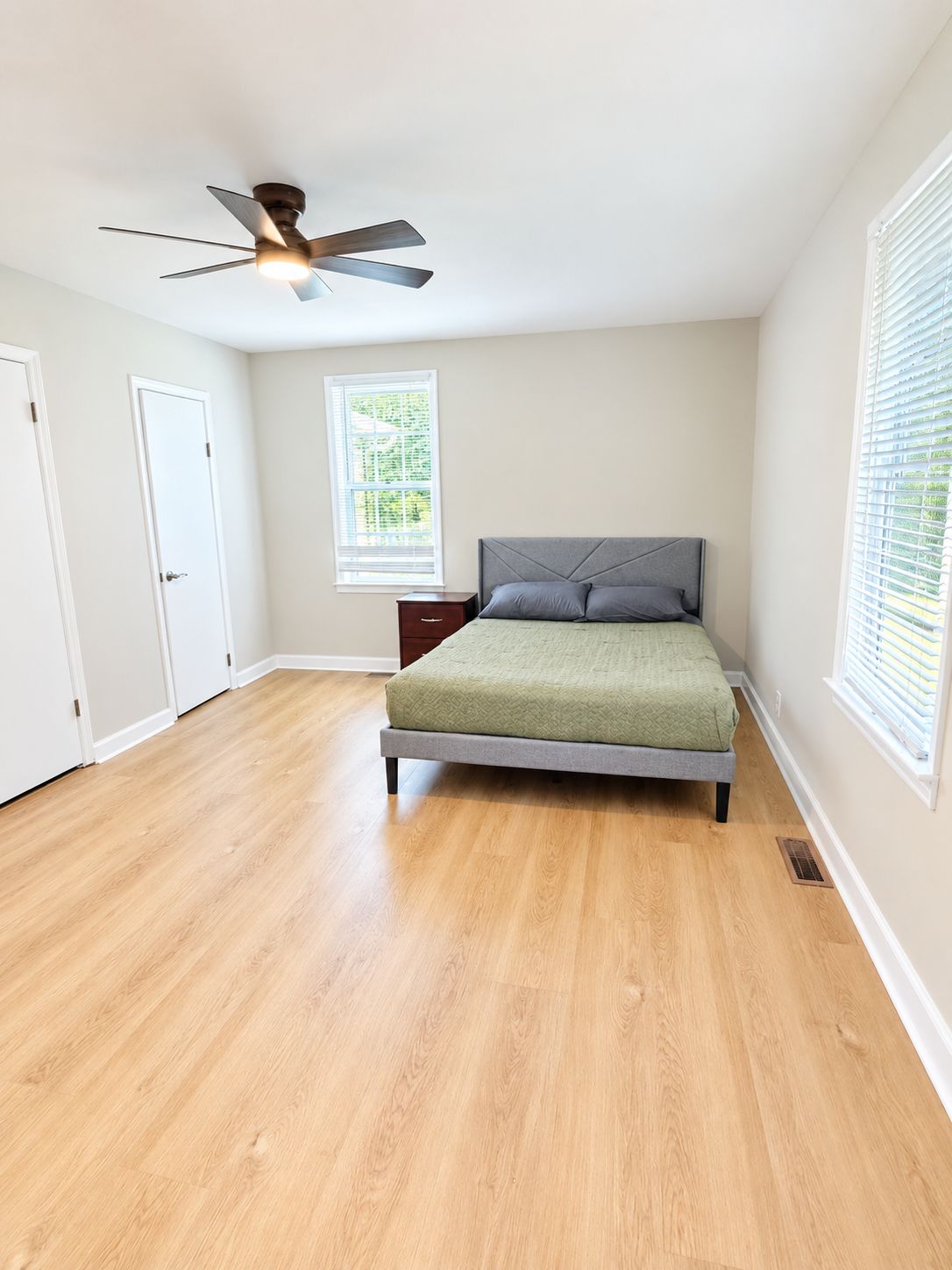 Une chambre à coucher avec un lit, un ventilateur de plafond, une fenêtre et une porte.