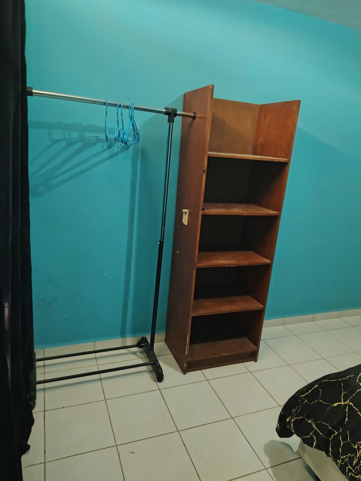 Una habitación con un armario de madera, un tendedero de metal y suelo de baldosas.
