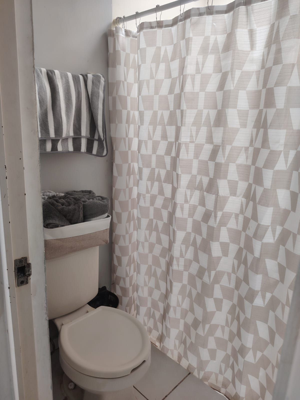 A bathroom with a toilet, a towel rack with striped towels, and a geometric patterned shower curtain.