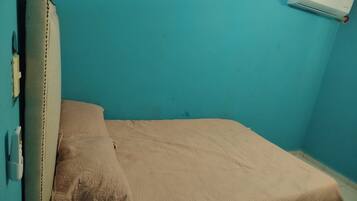 A single bed with a headboard, a wall-mounted air conditioner, and a power outlet on the wall.