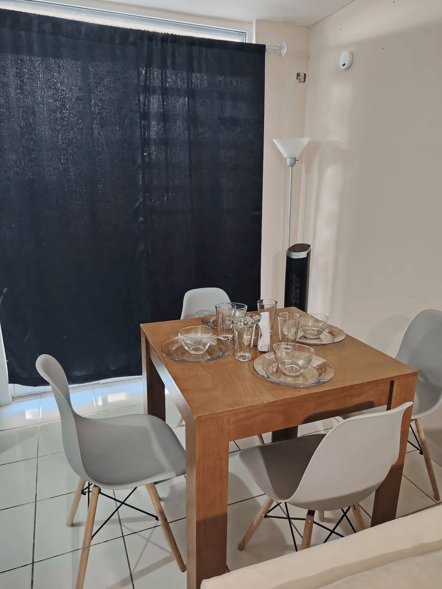 A dining area with a wooden table set for four, surrounded by white chairs.