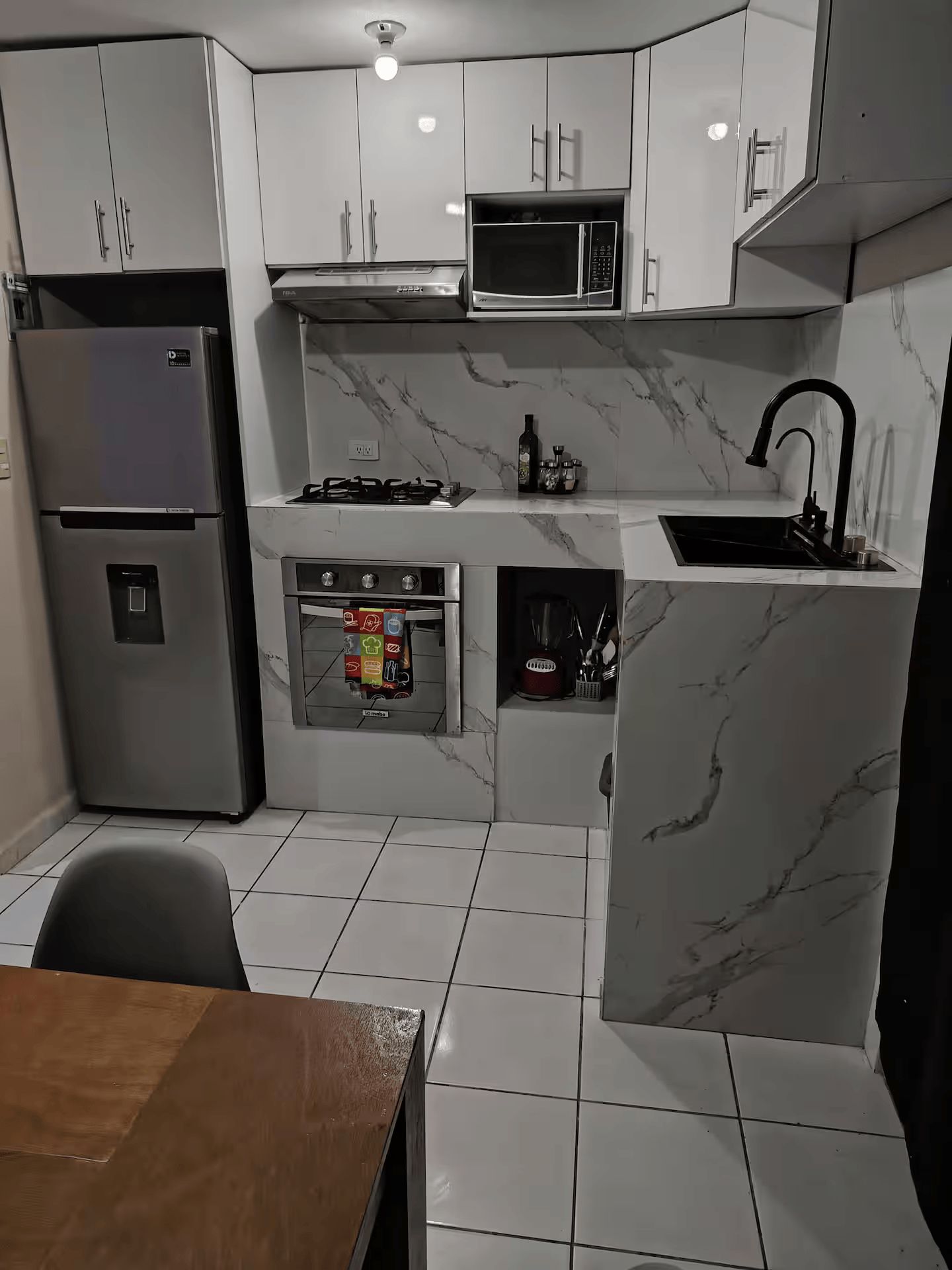 A compact kitchen with a refrigerator, microwave, stove, sink, and tiled floor.