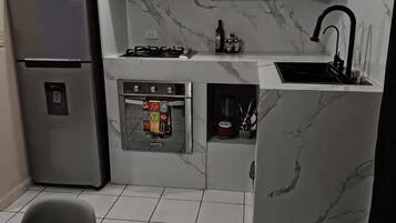 A compact kitchen with a refrigerator, microwave, stove, sink, and tiled floor.