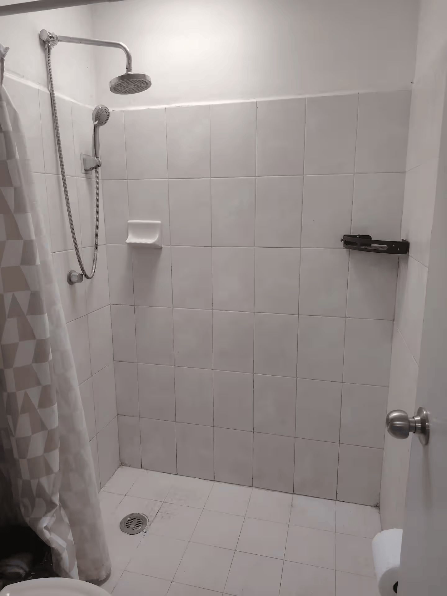 A small, enclosed shower area with a showerhead, a handheld showerhead, and a towel rack.