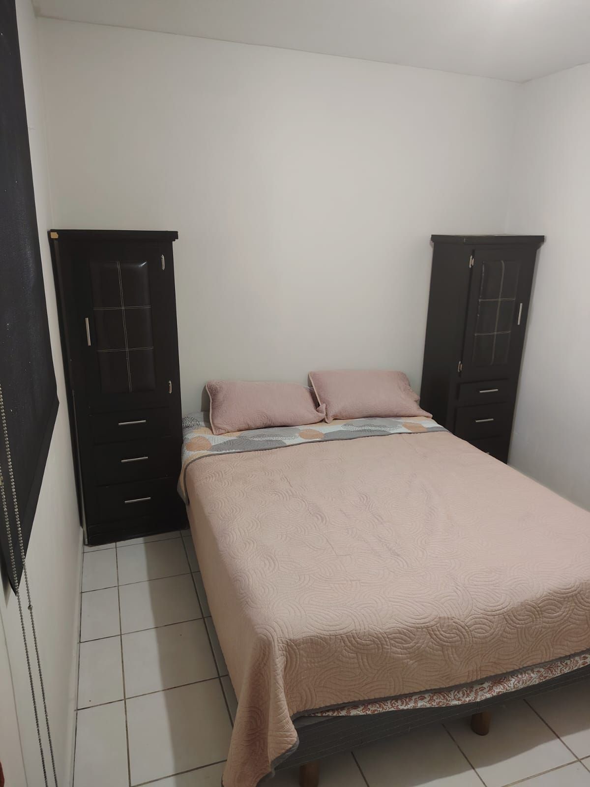 Une chambre à coucher avec un lit, deux armoires et un sol carrelé.