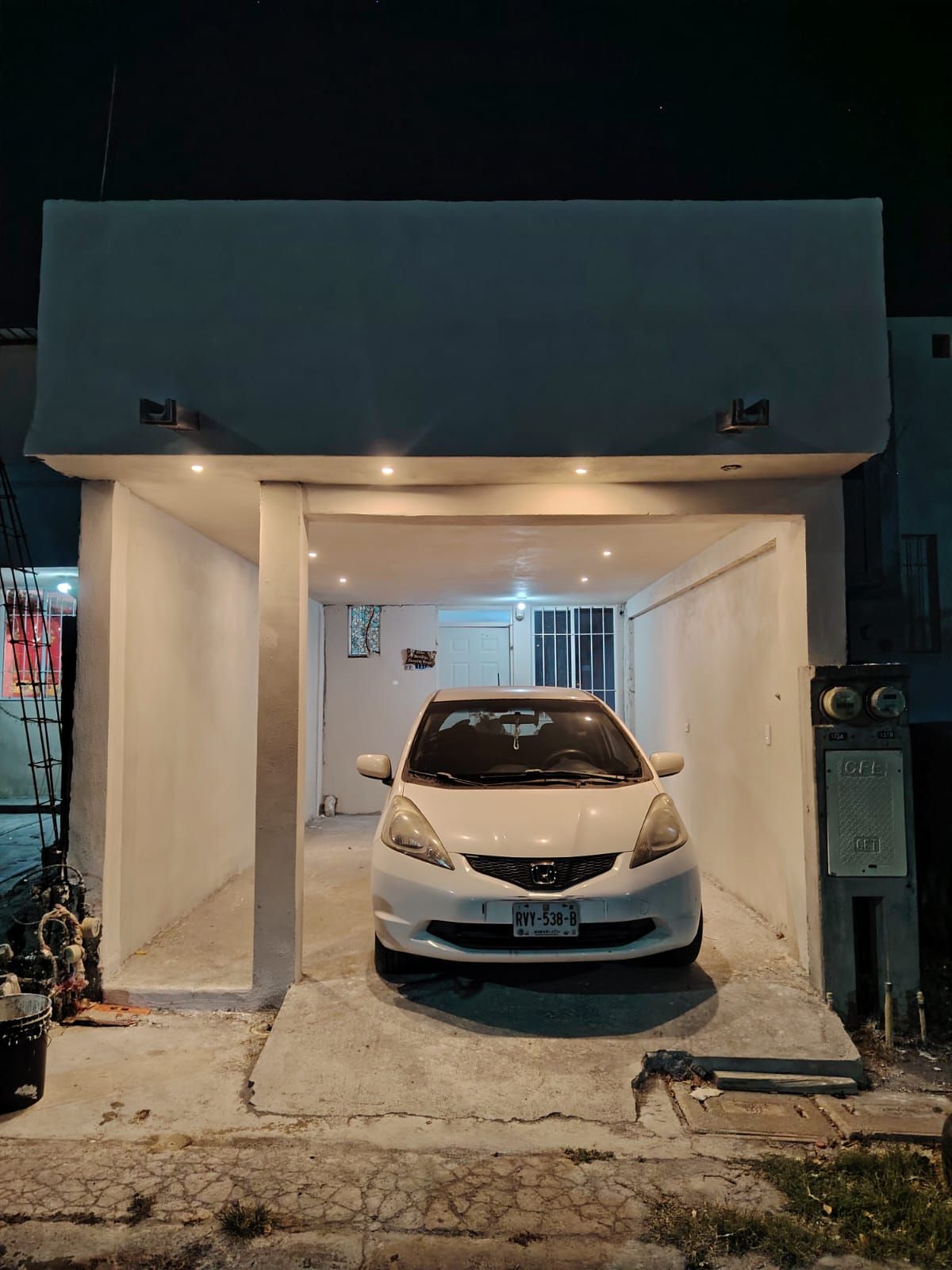 A white car parked inside a garage with a white door and a small window.