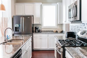 A modern kitchen with white cabinetry, stainless steel appliances, granite countertops, and a window providing natural light. - 4BR, 3.5BA beach retreat in Virginia Beach with parking, patio & kitchen. (Virginia Beach)