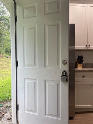 A white door with a keyhole and a lock, leading to a kitchen with white cabinets and a stainless steel appliance. - [5B/2B]-Spacious 5-bedroom house in quaint Quincy for working crews (Quincy)