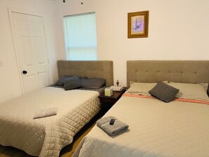 Une pièce avec deux lits, une fenêtre, une porte et un tableau encadré au mur.