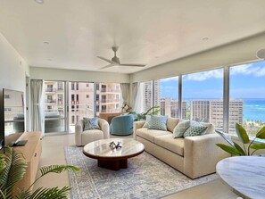 Ein modernes Wohnzimmer mit einem großen Fenster, einem Deckenventilator und Blick auf den Ozean.