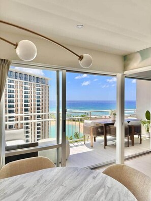 A hotel room with a balcony, a dining area, and a view of the ocean and a high-rise building. - 2-Bedroom 2-Bath Oceanfront House w/ Washer Dryer (Honolulu)