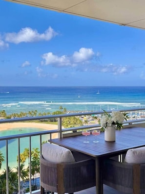 A balcony with a view of the ocean, a table with two chairs, and a vase with flowers. - 2-Bedroom 2-Bath Oceanfront House w/ Washer Dryer (Honolulu)