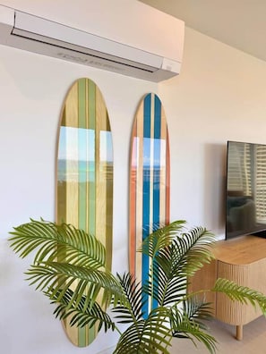 Two surfboards mounted on a wall, a television on a wooden stand, and a potted plant. - 2-Bedroom 2-Bath Oceanfront House w/ Washer Dryer (Honolulu)