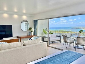 Ein modernes Hotelzimmer mit Balkon, Flachbildfernseher, Sofa und Essbereich mit Stühlen.