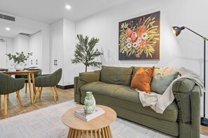 Uma sala de estar moderna com um sofá verde, uma mesa de centro e um quadro de flores na parede.