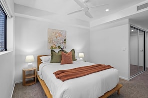 Ein modernes Schlafzimmer mit einem Bett, Kissen, einer Decke, einem Deckenventilator und einem Gemälde an der Wand.