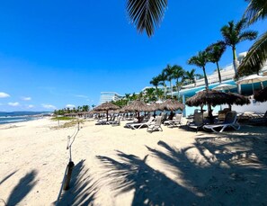 Una playa con tumbonas, palmeras y un cielo azul claro.