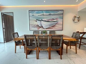 A dining area with a wooden table and wicker chairs, a large painting of a boat on the wall, and a welcome sign. - Maritima Playa Nvo Vallarta Elegante 3Rec/8p/Gym (Bucerías)