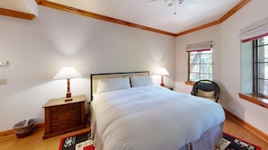 A bedroom with a bed, two bedside tables with lamps, a chair, a window with curtains, and a wooden floor. - Spruce Slopeside Ski-in Access (Beaver Creek)