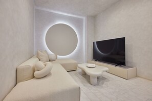A modern living room with a large flat-screen TV, a sofa, and a circular light fixture. - eni suite macchamachi (Chuo-ku)