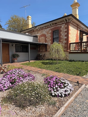 A two-story house with a brick facade, a covered porch, and a garden with flowering plants.