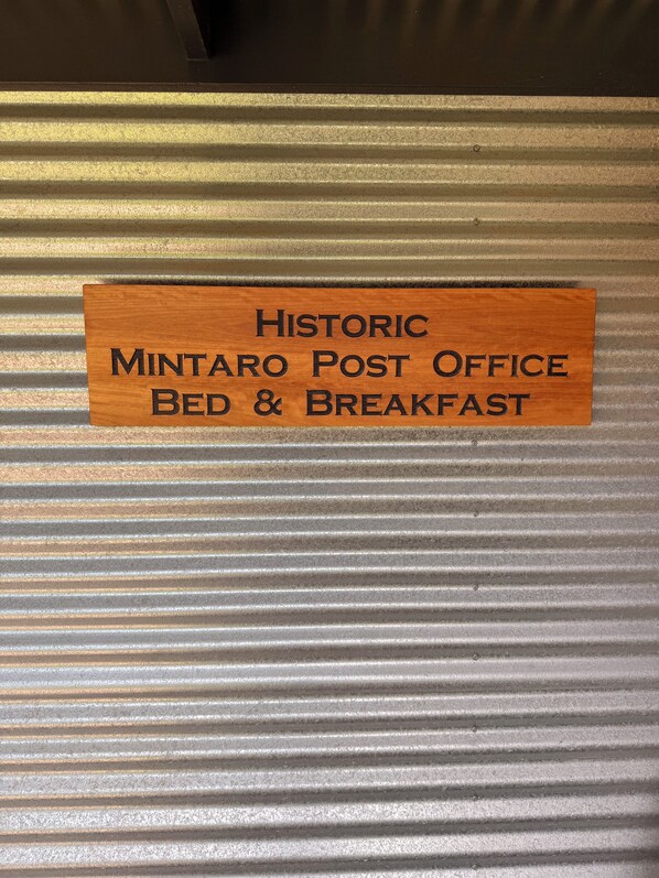 A wooden sign with the text 'Historic Mintaro Post Office Bed & Breakfast' on a corrugated metal background.