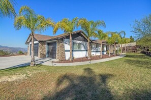 A single-story house with a stone facade, a garage, and a well-maintained lawn with palm trees. - Luxury Escape | Heated Pool/Spa • Views + Events (Alpine)