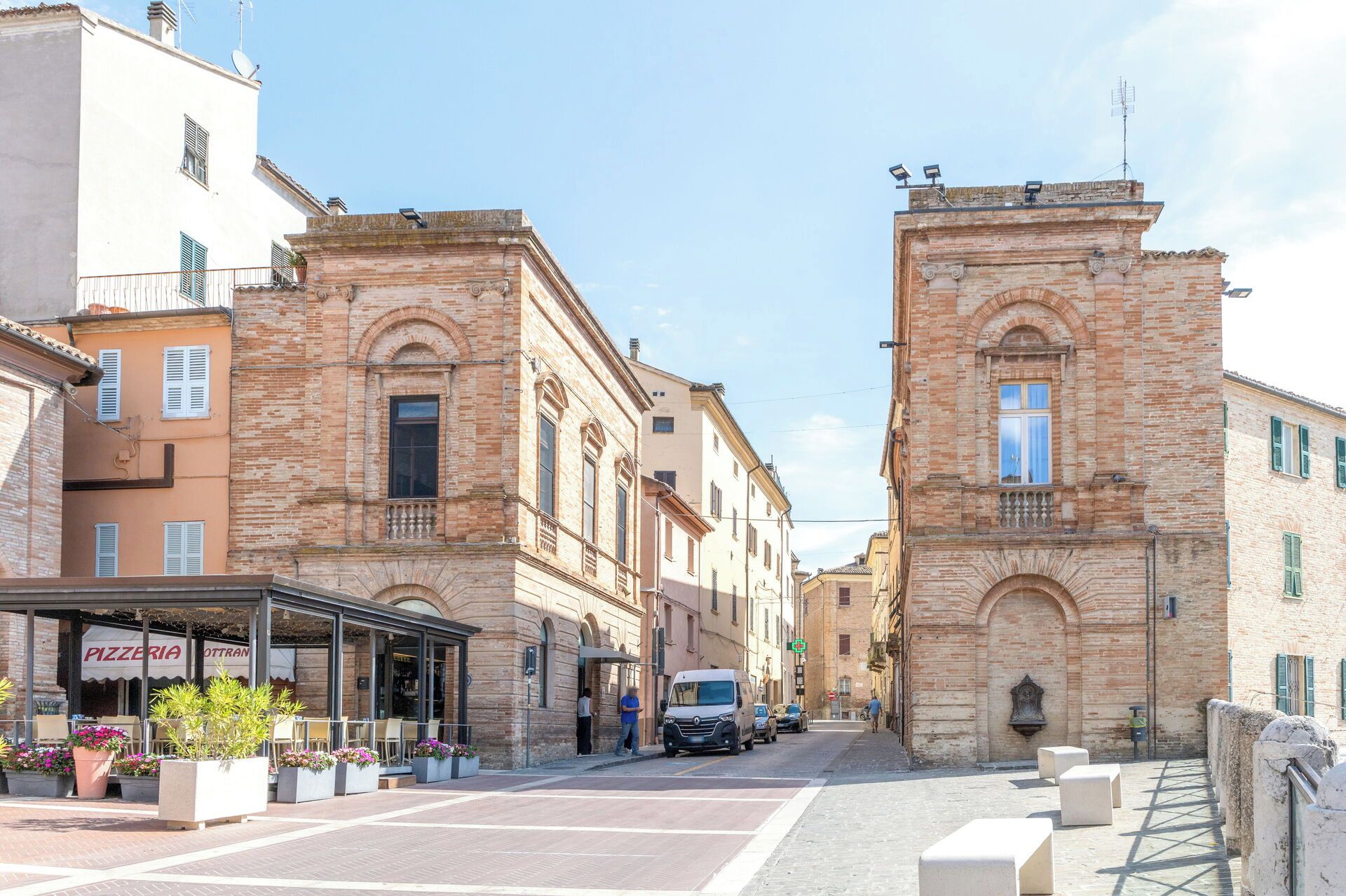 A street with buildings, a pizzeria, and a parked van.