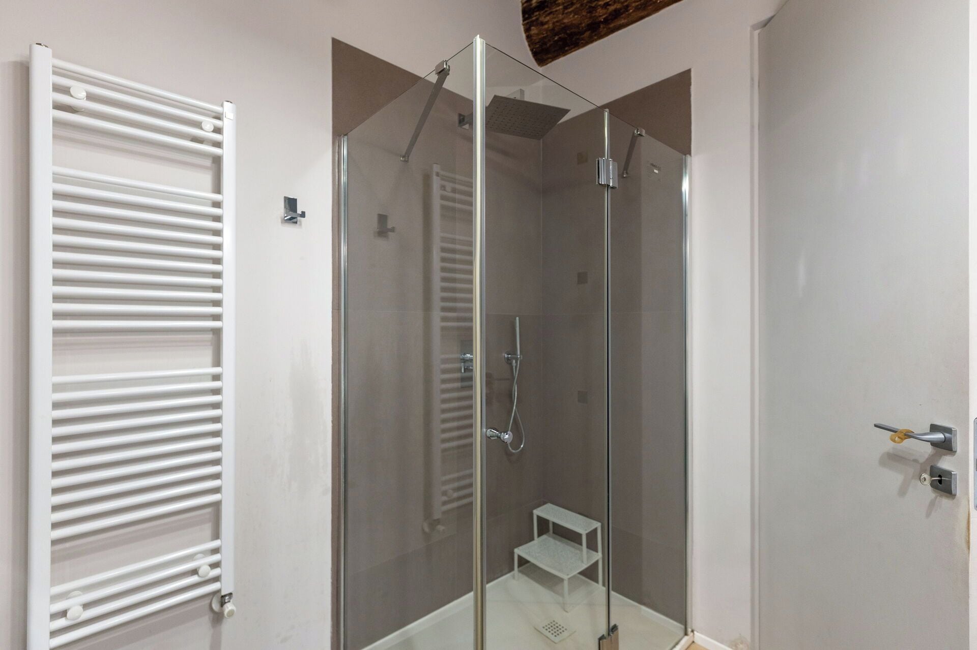 Ein modernes Badezimmer mit einer gläsernen Duschkabine, einem weißen Handtuchhalter und einer kleinen Ablagefläche.