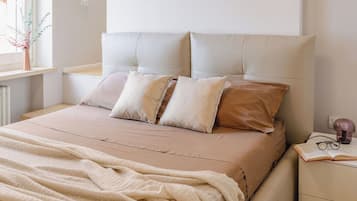 A bed with a headboard, multiple pillows, a blanket, and a bedside table with glasses and a book.