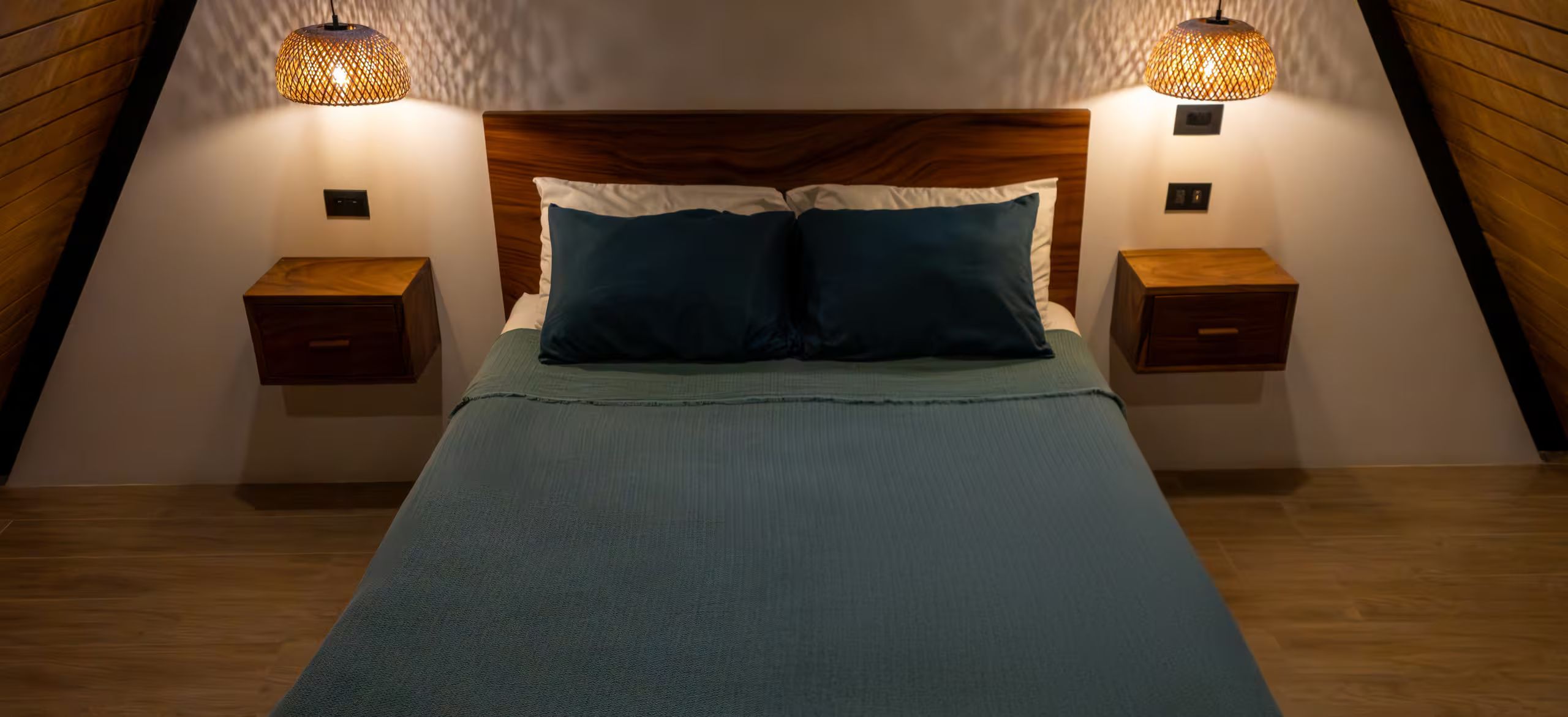 Une chambre à coucher avec une tête de lit en bois, deux tables de chevet et un lit recouvert d’une couverture bleue.
