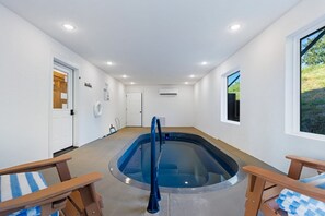 Um espaço de spa com uma banheira de hidromassagem, duas cadeiras de madeira, uma porta e uma janela.