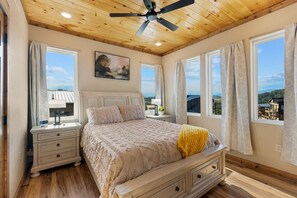 Ein Schlafzimmer mit einem Bett, Nachttischen, einem Deckenventilator und großen Fenstern mit Vorhängen.