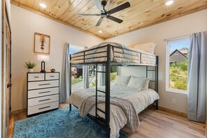Quarto com beliche, ventoinha no teto, cômoda e janela com cortinas.