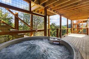 Ein Whirlpool auf einer Holzterrasse mit Blick auf Bäume und einen klaren Himmel.