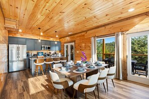 Eine moderne Küche mit Edelstahlgeräten, ein Essbereich mit Holztisch und -stühlen sowie große Fenster mit Blick ins Freie.
