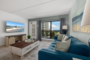 Ein modernes Wohnzimmer mit großem Fernseher, einer Couch und Blick auf Strand und Häuser.