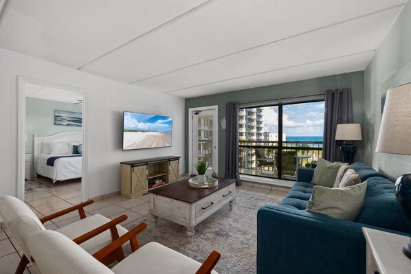 Een moderne hotelkamer met balkon, een bed, een zithoek met een bank en stoelen, en een aan de muur bevestigde televisie.