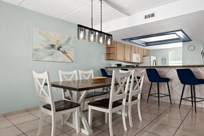 A modern kitchen with a dining area, featuring a table with chairs, a pendant light, and a painting on the wall. - Saida III #606 | Beachfront Condo • 3 Pools • Tennis & Pickleball (South Padre Island)