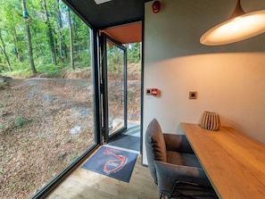A modern interior with a wooden dining table, a cushioned bench, and a large window offering a forest view. - The Blooming Refuge - Hydrangea Cabin (La Roche-en-Ardenne)