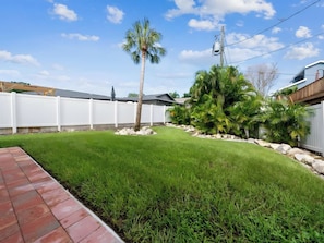 A well-maintained backyard with a lawn, palm trees, a white fence, and a brick pathway. - Two-Story 3BR with Pool Table and Private Yard (St. Petersburg)