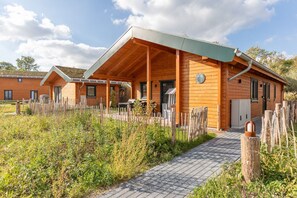 Eine Holzhütte mit überdachter Veranda, einem gepflasterten Weg und einem umzäunten Gartenbereich.
