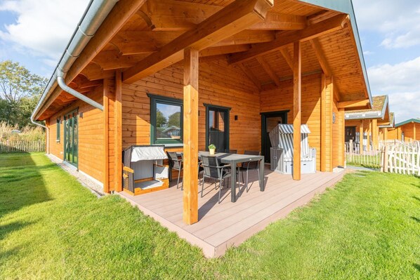 Eine Holzhütte mit überdachter Veranda, Sitzgelegenheiten im Freien und Blick auf die umliegende Landschaft.