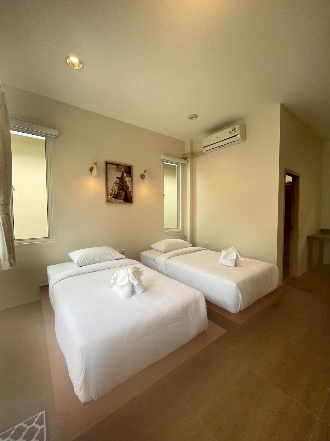 A hotel room with two beds, a painting on the wall, an air conditioning unit, and a window with curtains.