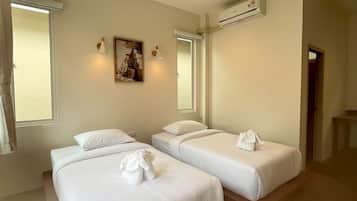 A hotel room with two beds, a painting on the wall, an air conditioning unit, and a window with curtains.