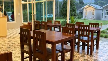 A covered outdoor dining area with a patterned floor, wooden tables and chairs, and large windows offering a view of the surrounding landscape.